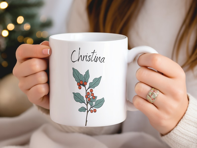 May include: White ceramic mug with a green holly sprig and red berries design. The mug has the name "Christina" written in black cursive on the front.