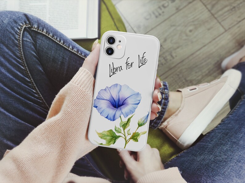 Puede incluir: Una funda de tel&eacute;fono blanca con una ilustraci&oacute;n de acuarela de una flor de gloria de la ma&ntilde;ana azul con hojas verdes y el texto "Libra for Life" en escritura negra. La funda est&aacute; en las manos de una persona.