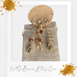 May include: A pair of gold wire hair coils with amber beads and shell accents. The coils are displayed in a small burlap bag.