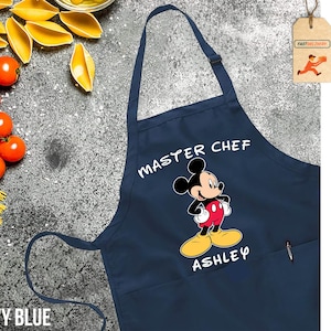 May include: Navy blue apron with a white pocket and a Mickey Mouse graphic. The apron says "Master Chef" and "Ashley" in white text.