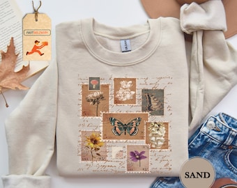 May include: A beige sweatshirt with a vintage-inspired design featuring a collage of postage stamps with floral and butterfly illustrations. The text "SAND" is visible in the lower right corner of the image.