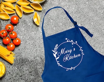 May include: A royal blue kitchen apron with a white circle design featuring the text "Mary's Kitchen" and a floral wreath.