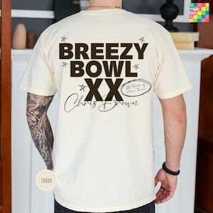 a person wearing a white t-shirt with a graphic design featuring the text "BREEEZY BOWL XX" and the name "Chris Brown" along with a small text that says "20 Years of Chris Brown".