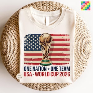 A white t-shirt with a graphic design featuring the FIFA World Cup trophy and the text "One Nation, One Team USA - World Cup 2026" printed on it.
