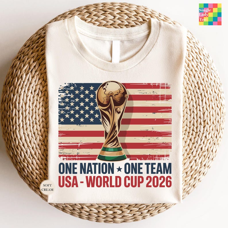 A white t-shirt with a graphic design featuring the FIFA World Cup trophy and the text "One Nation, One Team USA - World Cup 2026" printed on it.