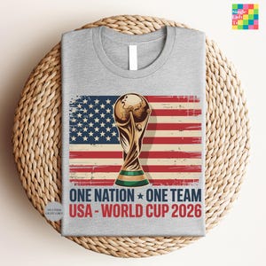 A gray t-shirt with a graphic design featuring the FIFA World Cup trophy and the text "One Nation, One Team USA - World Cup 2026" printed on it.