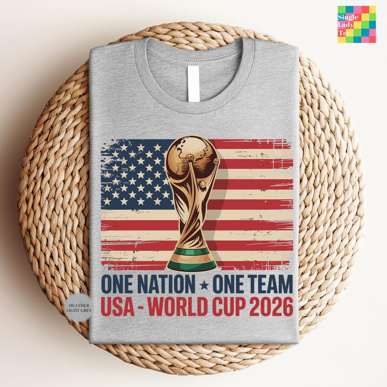 A gray t-shirt with a graphic design featuring the FIFA World Cup trophy and the text "One Nation, One Team USA - World Cup 2026" printed on it.