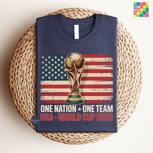 A navy blue t-shirt with a graphic design featuring the FIFA World Cup trophy and the text "One Nation, One Team USA-World Cup 2026" printed on it.