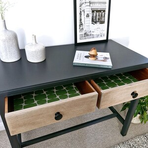 May include: A black console table with two drawers. The drawers have a wood front and a green patterned liner. A book titled "Remarkable Interiors" is on top of the table.