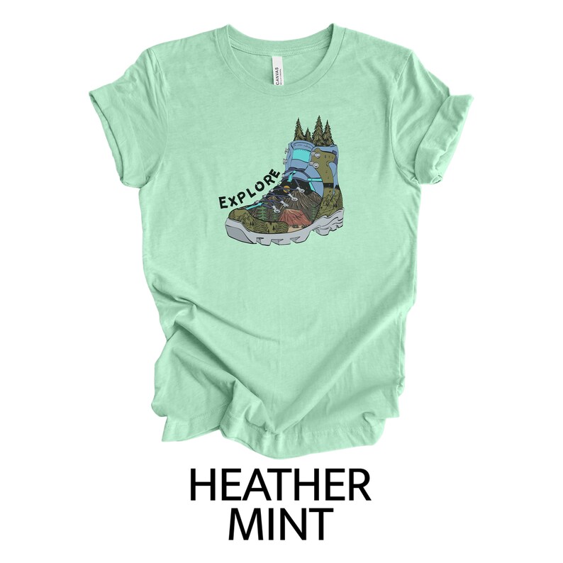 May include: A light green t-shirt with a graphic of a hiking boot with a mountain scene inside. The text "EXPLORE" is printed above the boot.