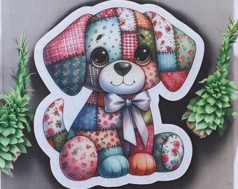 Pode incluir: Um autocolante colorido de um cão de retalhos com olhos grandes e expressivos e um laço branco. O corpo do cão é feito de vários padrões de tecido em tons de rosa, azul, vermelho e verde. O autocolante tem uma borda branca.