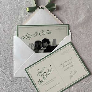 May include: A white envelope with a scalloped edge and green ribbon containing a save the date card featuring a black and white photo of a couple and the text Ally & Collin. A matching postcard with the text Save the Date! and Chicago, Illinois.