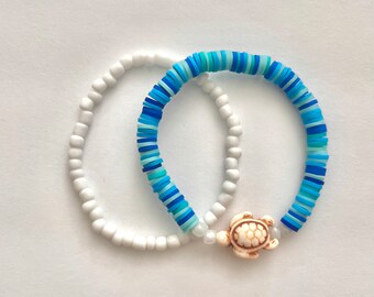 May include: Two bracelets, one white and one with blue and turquoise beads, with a small white turtle charm.
