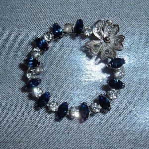 May include: A silver brooch with a blue and white rhinestone circle and a silver flower design.