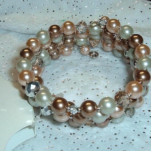 May include: A multi-strand wrap bracelet featuring alternating round beads in shades of cream, light pink, and metallic copper, interspersed with small clear faceted crystal accents. A white tag with the text Croft & Barrow is visible.