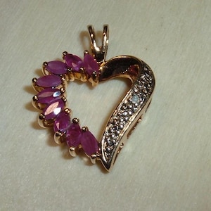 May include: A gold heart-shaped pendant with a row of small diamonds on one side and a row of pink gemstones on the other side.