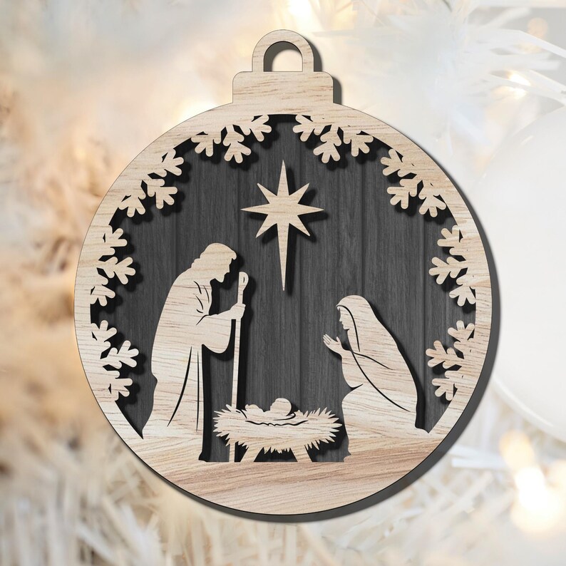 May include: Wooden Christmas ornament featuring a Nativity scene. The ornament is round with a snowflake border and a loop for hanging. The scene depicts Mary, Joseph, and baby Jesus under a star. The background is a dark wood grain.