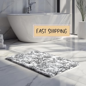 May include: A white bath mat with a black and white floral pattern. The mat is in a bathroom with a white bathtub and a white tiled floor. The text "FAST SHIPPING" is visible in the image.