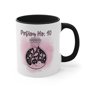 May include: White ceramic mug with a black rim and handle. The mug features a pink watercolor background with a black and white illustration of a potion bottle with a cork stopper. The text "Potion No. 10" is printed in black on the mug.