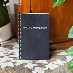 May include: A black spiral bound journal with the text "EVOLVING HABITS JOURNAL" printed in white on the front cover.
