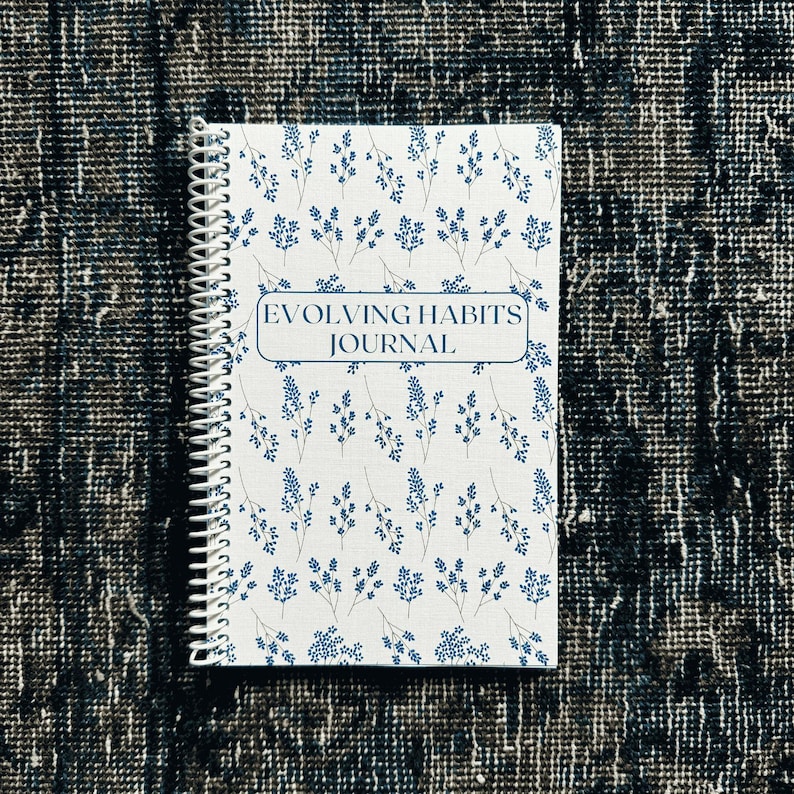 May include: A white spiral bound journal with a blue floral pattern and the text "Evolving Habits Journal" on the front cover.