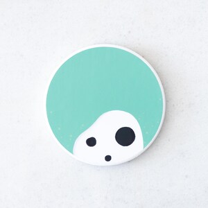 Puede incluir: Un posavasos redondo con fondo turquesa y una forma abstracta blanca con tres puntos negros. El dise&ntilde;o es simple y moderno, adecuado para varios estilos de decoraci&oacute;n del hogar.