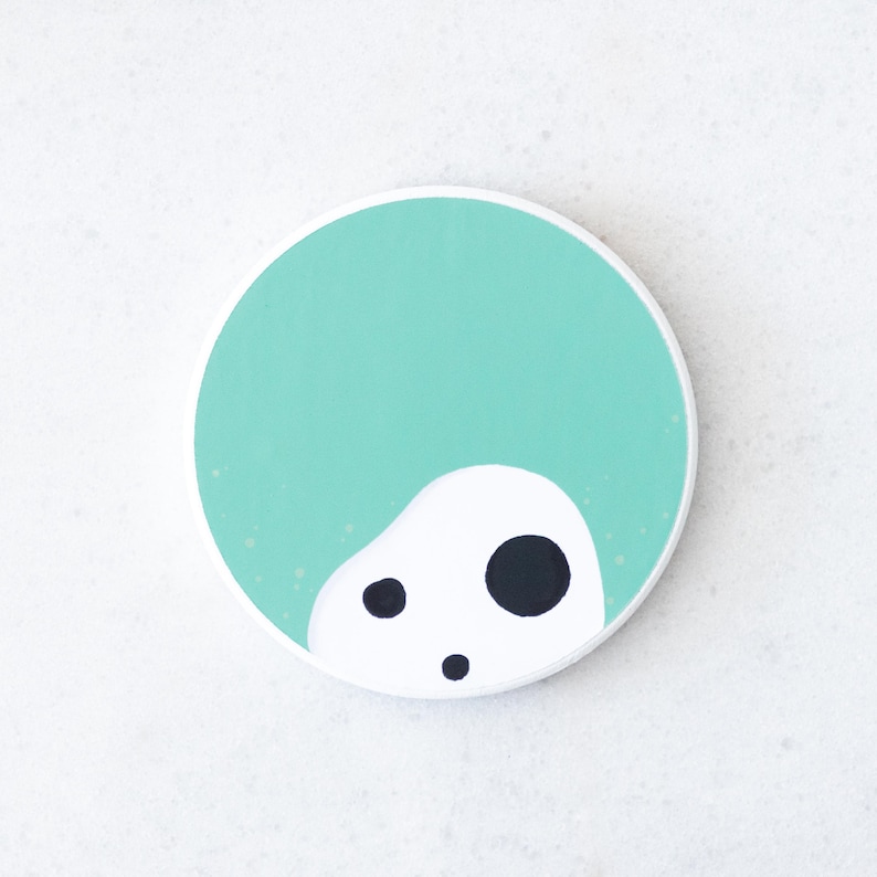 Puede incluir: Un posavasos redondo con fondo turquesa y una forma abstracta blanca con tres puntos negros. El dise&ntilde;o es simple y moderno, adecuado para varios estilos de decoraci&oacute;n del hogar.