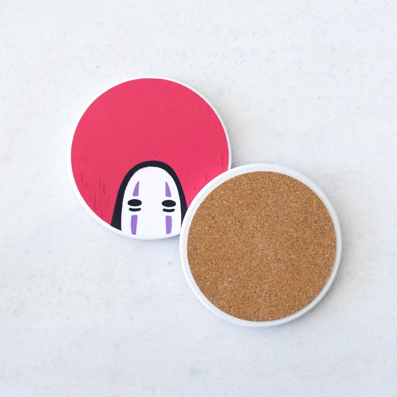 Puede incluir: Dos posavasos redondos. Uno presenta un fondo rojo con una cara de personaje blanco y negro. El otro tiene una base de corcho y un borde blanco. Los posavasos est&aacute;n dise&ntilde;ados con un tema de dibujos animados.
