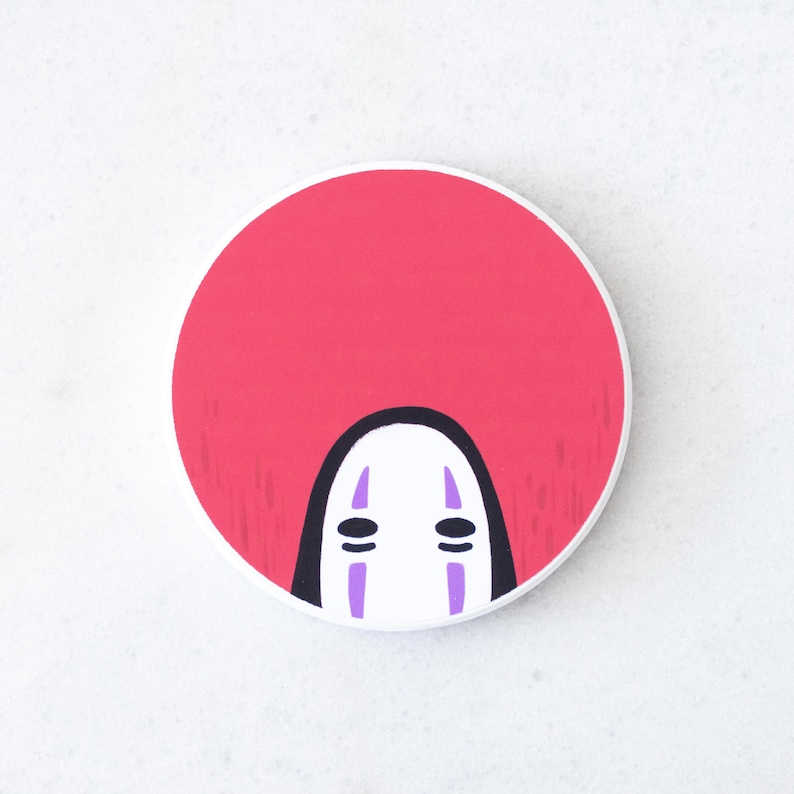 Puede incluir: Un bot&oacute;n redondo blanco con un fondo rosa y una cara estilizada de la pel&iacute;cula de animaci&oacute;n El Viaje de Chihiro. La cara tiene una base blanca con ojos negros y l&iacute;neas verticales moradas.