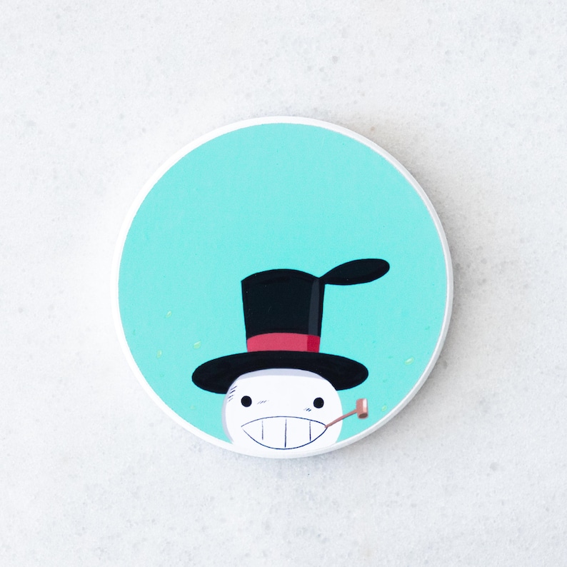Puede incluir: Un posavasos redondo y blanco con un mu&ntilde;eco de nieve de dibujos animados con sombrero de copa negro, banda roja y pipa. El mu&ntilde;eco de nieve tiene una amplia sonrisa y est&aacute; sobre un fondo azul claro.