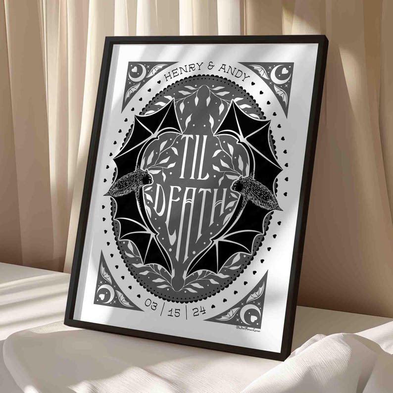 This photo shows the grey, white and black version of this art. The art features two bats. Their wings form the shape of a heart with the words til death framed the center of the art. Crescent moons, botanical illustrations and small hearts surround the bats. The couple’s first names and anniversary date are arched on the top and bottom on the art in a folk-style font