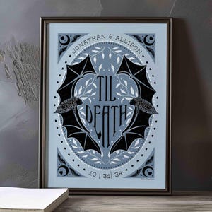 This photo shows the dusty blue and black version of this art. The art features two bats. Their wings form the shape of a heart with the words til death framed the center of the art. Crescent moons, botanical illustrations and small hearts surround the bats. The couple’s first names and anniversary date are arched on the top and bottom on the art in a folk-style font