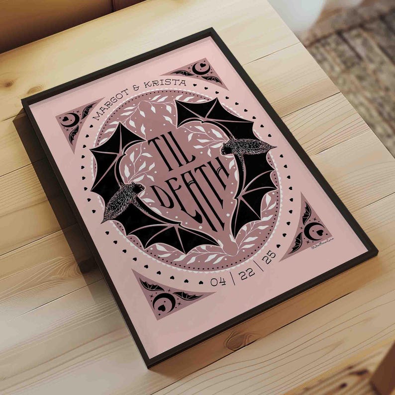 This photo shows the dusty rose pink and black version of this printable wall art. The art features two bats. Their wings form the shape of a heart with the words til death framed the center of the art. Crescent moons, botanical illustrations and small hearts surround the bats. The couple’s first names and anniversary date are arched on the top and bottom on the art in a folk-style font