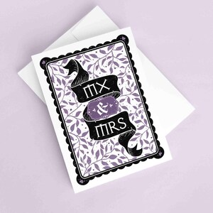 Puede incluir: Una tarjeta de felicitación con un borde negro festoneado y un sobre blanco. La tarjeta presenta una pancarta con las palabras "MX & MRS" en negro, con un fondo floral púrpura.