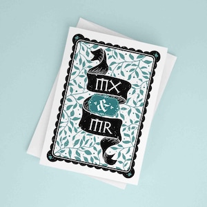 Puede incluir: Una tarjeta de felicitación con borde negro y diseño floral turquesa y blanco. La tarjeta presenta una pancarta negra con el texto "MX & MR" y un acento turquesa. La tarjeta está sobre un sobre blanco.