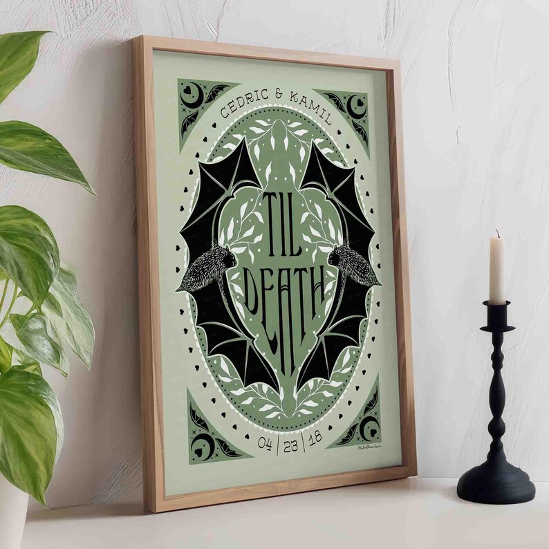 This photo shows the sage green and black version of this printable wall art. The art features two bats. Their wings form the shape of a heart with the words til death framed the center of the art. Crescent moons, botanical illustrations and small hearts surround the bats. The couple’s first names and anniversary date are arched on the top and bottom on the art in a folk-style font