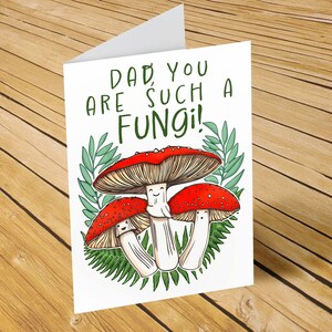 Printable 5x7 card that has 3 hand illustrated toadstool mushrooms with smiling faces and green leaves behind them. The words, "Dad, you are such a fungi!" are above the toadstools.