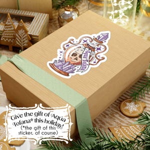 Photo shows the sticker on a present box with the text: “Give the gift of Aqua Tofana* this holiday! (*the gift of this sticker, of course)”