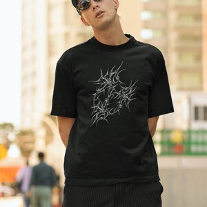 May include: A person wearing a black t-shirt with a white graphic design of a stylized heart with thorns. The t-shirt has the text "CYBERHEARTS COLLECTIVE" on the top left corner. The person is wearing a black cap and sunglasses.
