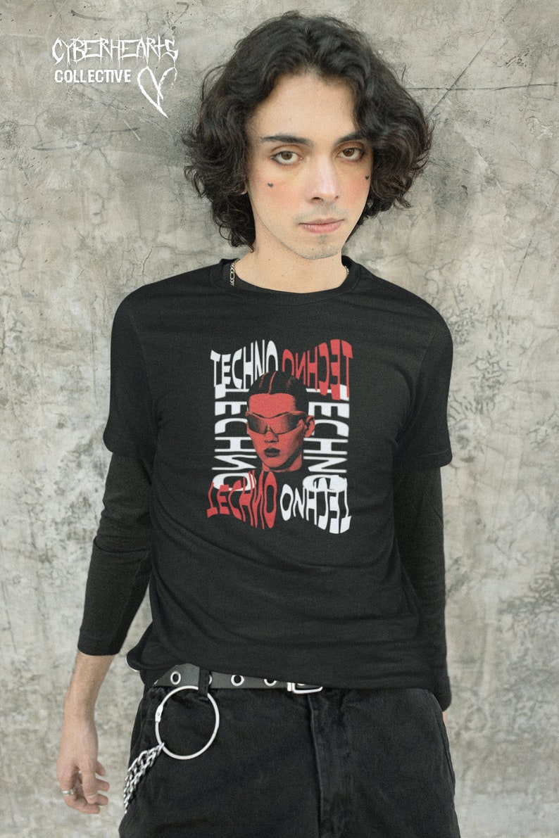 May include: A black long-sleeve t-shirt with a red and white graphic print of a person wearing sunglasses and the word "techno" repeated multiple times. The person has a black and red face.