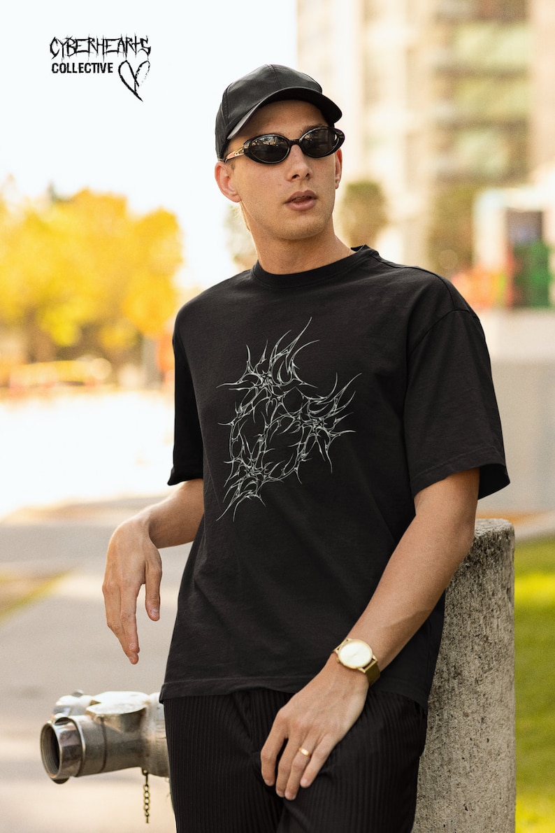 May include: A black t-shirt with a white graphic of a stylized heart with barbed wire. The t-shirt has a crew neck and short sleeves. The text "CYBERHEARTS COLLECTIVE" is visible in the top left corner of the image.