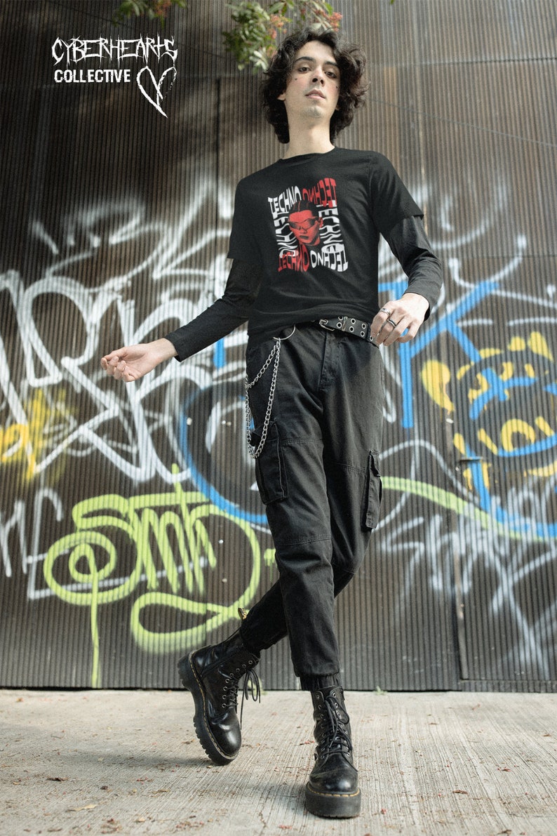 May include: A person wearing a black long-sleeved shirt with a red and white graphic print that says "Techno Omnia" and black cargo pants. The person is wearing black combat boots and a silver chain.