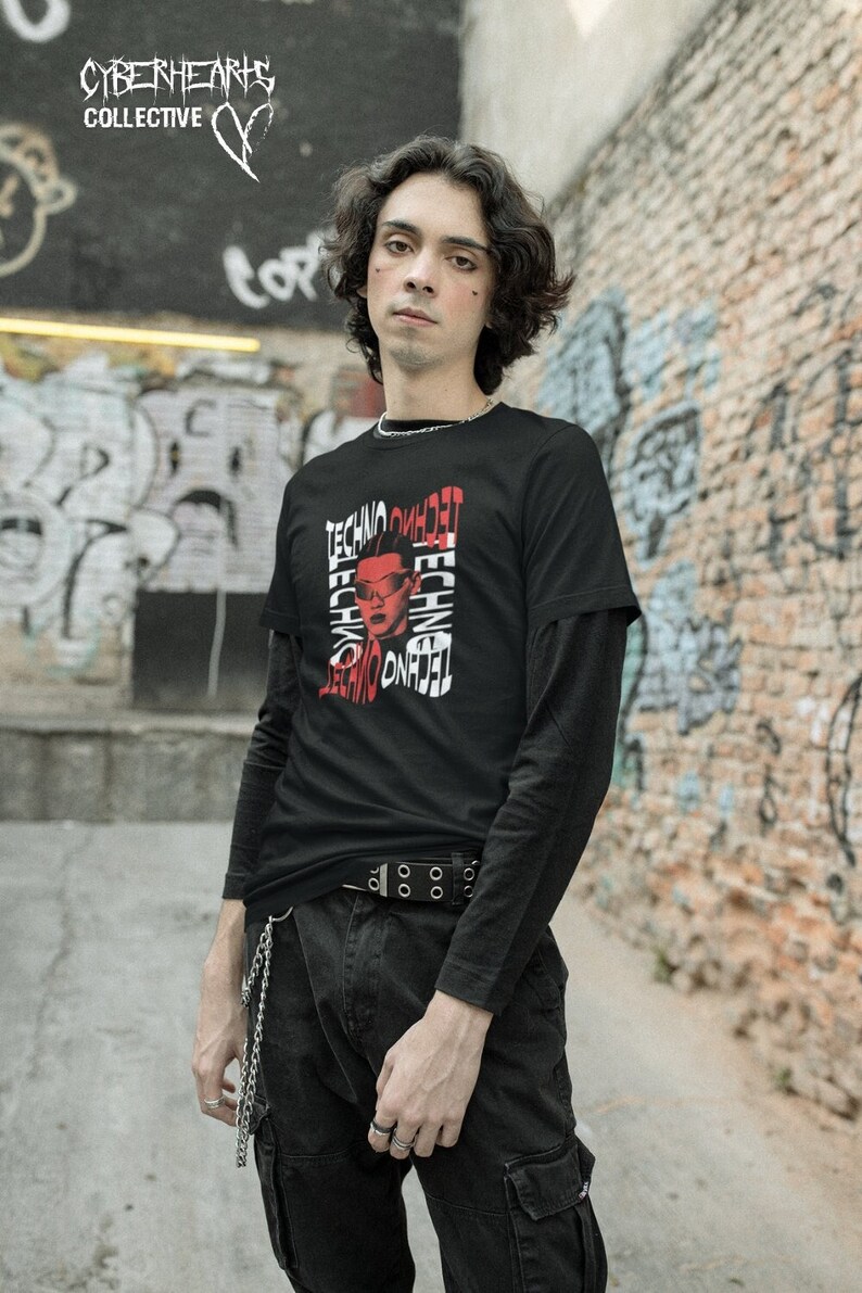 May include: A person wearing a black long-sleeved shirt with a red and white graphic print of a person's face with the word "Techno" repeated multiple times. The person is wearing black pants with a silver chain and a black belt with silver buckles.