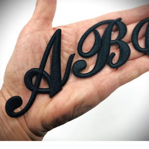May include: Black iron-on letters in a cursive font. The letters are A, B, and C. The letters are on a hand.