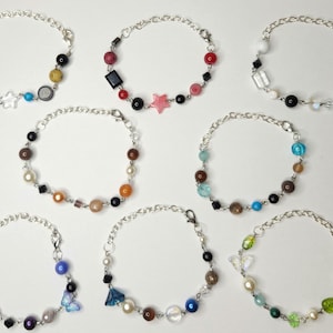 May include: Ten silver chain bracelets with colorful beads and charms. Each bracelet features a different combination of colors and charms, including stars, butterflies, and geometric shapes.