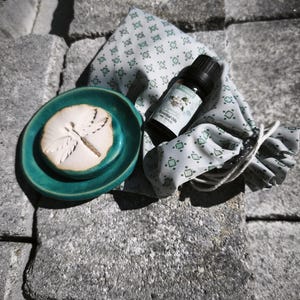 Könnte beinhalten: Eine kleine türkisfarbene Keramikschale mit einem Libellenrelief, eine dunkle Glasflasche mit ätherischen Ölen und einem Etikett mit der Aufschrift Jasmine Essential Oils 10ml 1/3 fl oz sowie ein heller Stoffbeutel mit grünem Muster.