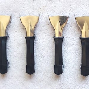May include: Eight metal scrapers with gold-coloured blades and black handles. The blades are shaped like an inverted U. The handles are cylindrical and have a small metal clip. The scrapers are arranged in a row.
