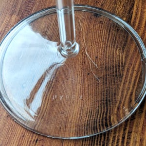 May include: A clear glass Pyrex lid with a stem, on a wooden surface. The circular lid has a raised rim and the word "PYREX" is visible. The stem is attached to the centre of the lid.