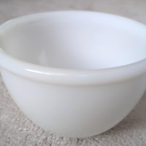 Peut inclure: Un petit bol rond blanc avec un bec verseur. Le bol est en verre opaque et possède un bord lisse et arrondi. Le bol est vide et repose sur une surface neutre.