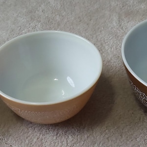 Puede incluir: Tres cuencos de cerámica de diferentes tamaños. Los cuencos tienen un exterior marrón claro con un estampado floral blanco cerca de la base y un interior blanco. Los cuencos están dispuestos de menor a mayor.